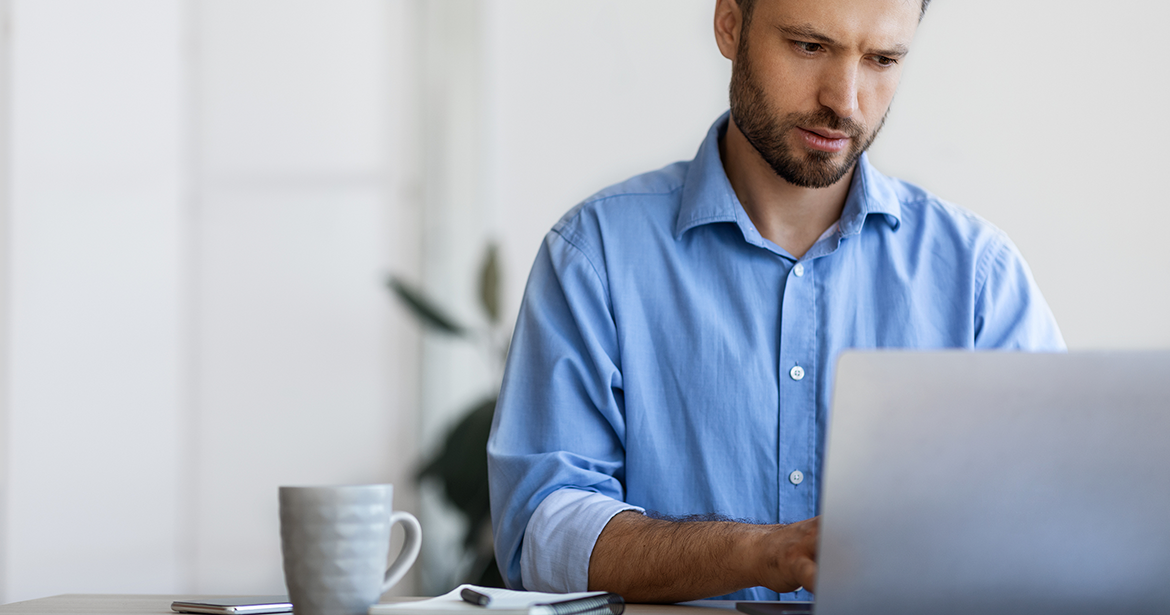 Man sitting at desk looking quizzically at laptop